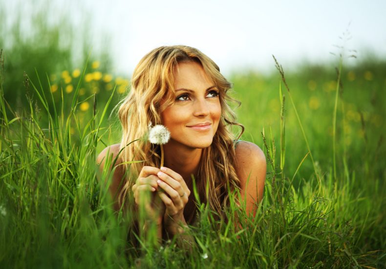 草原でたんぽぽの綿毛をもつ女性