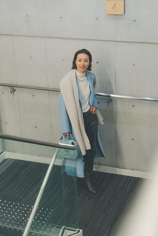 白のタートルニットと黒デニムパンツに水色のロングコートをはおったモデル写真