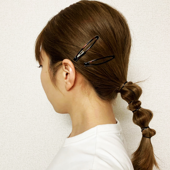 髪をつまんで大小のポンポンをつくり、サイドにヘアピンを2つつけたひとつ結びの横顔写真