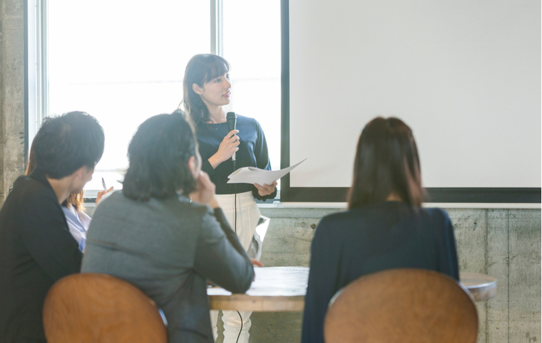 スクリーンの前で司会進行中の女性の写真