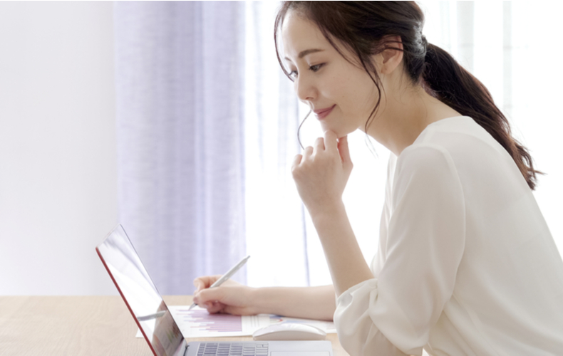 ペンを片手にノートPCを見ながら仮名が得ている女性の写真