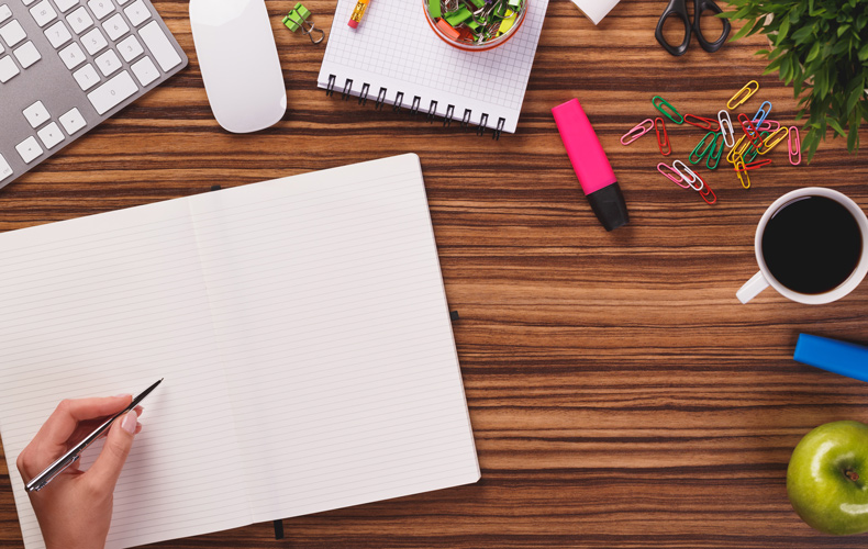 デスクでノートに何か書こうとしている手元の写真