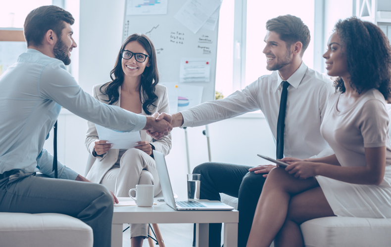 握手する男性ビジネスマンと、同席する女性ビジネスマン2人