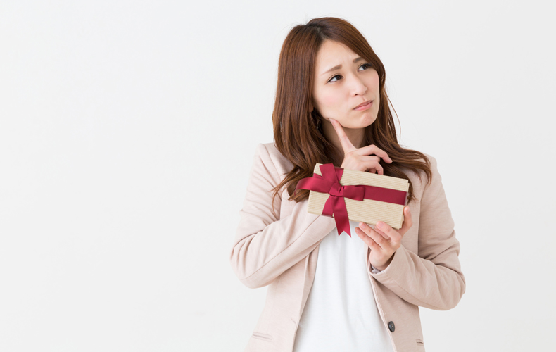 プレゼントの箱を片手に持ち、頬に指をあてて考え事をする女性
