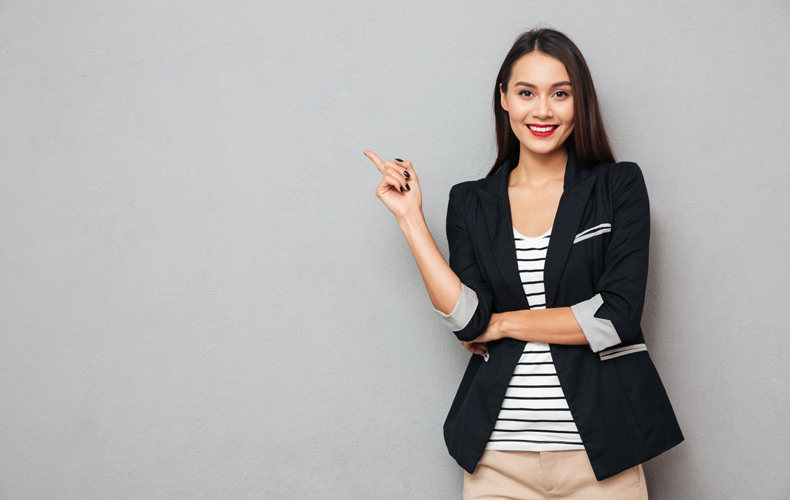 ジャケット姿の女性が人差し指を立てるポーズをとっている