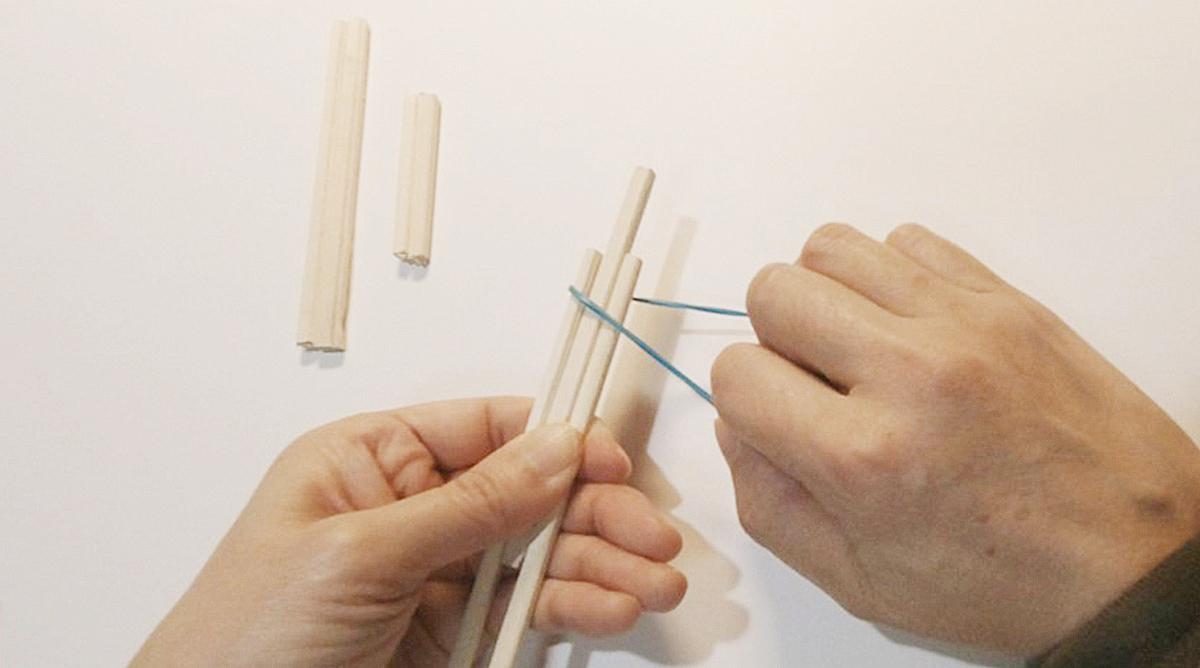 割った割り箸の間に半分に切った割り箸を輪ゴムでとめている写真 指は向こう側を向いている