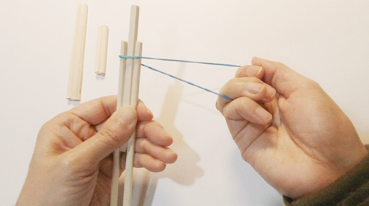 割った割り箸の間に半分に切った割り箸を輪ゴムでとめている写真 指はこちら側を向いている