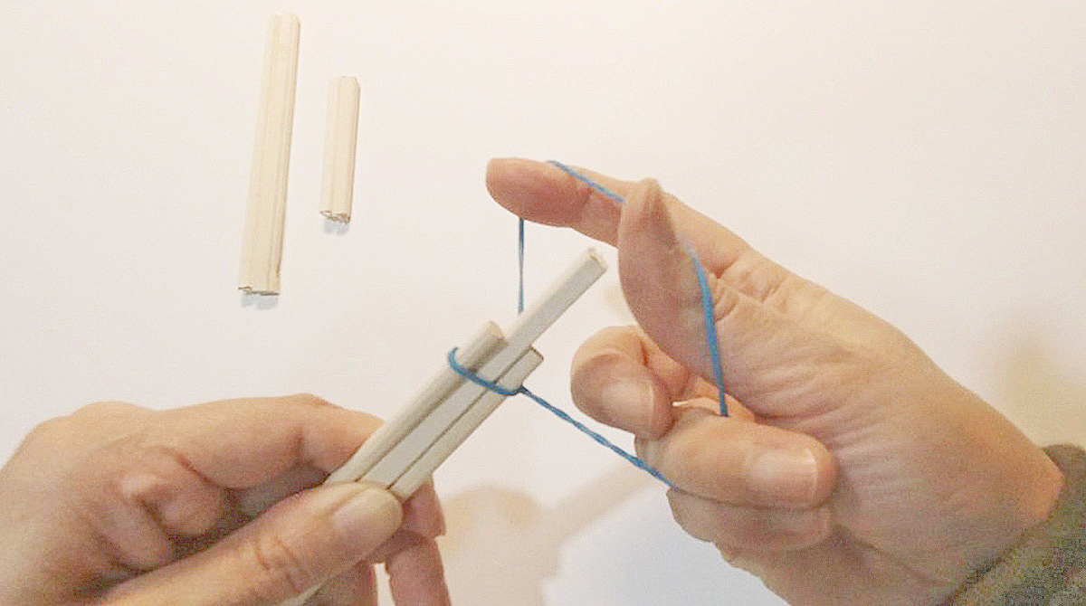 割った割り箸の間に半分に切った割り箸を輪ゴムでとめている写真 人差し指と親指で輪ゴムを広げている