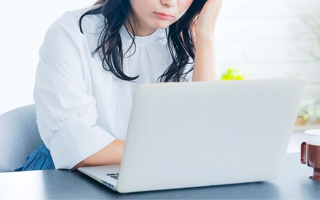 ノートパソコンの前で悩んでいる女性の写真