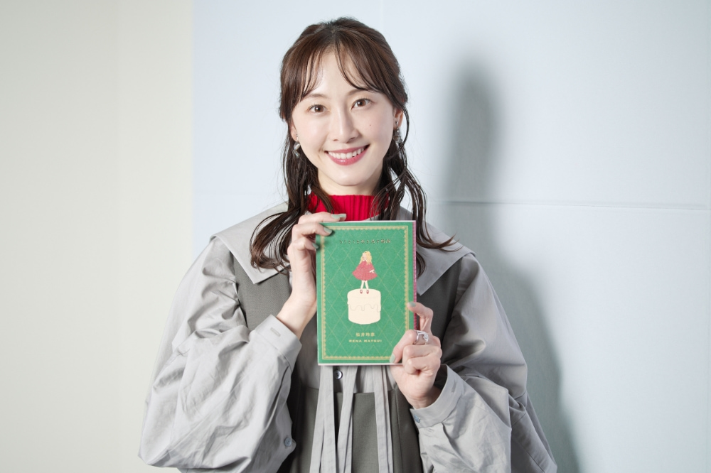 エッセイを手に持って微笑む松井玲奈さんの写真
