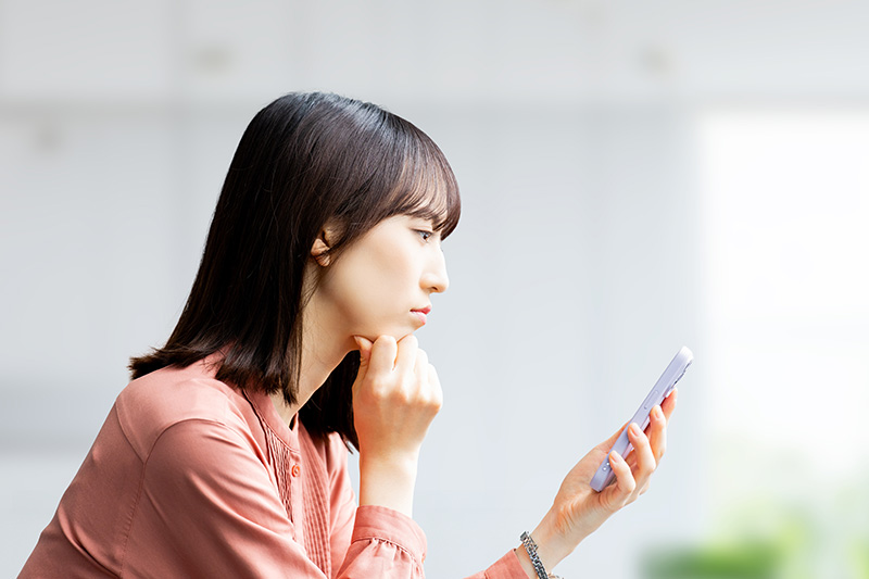 スマートフォンを見て考える若い女性