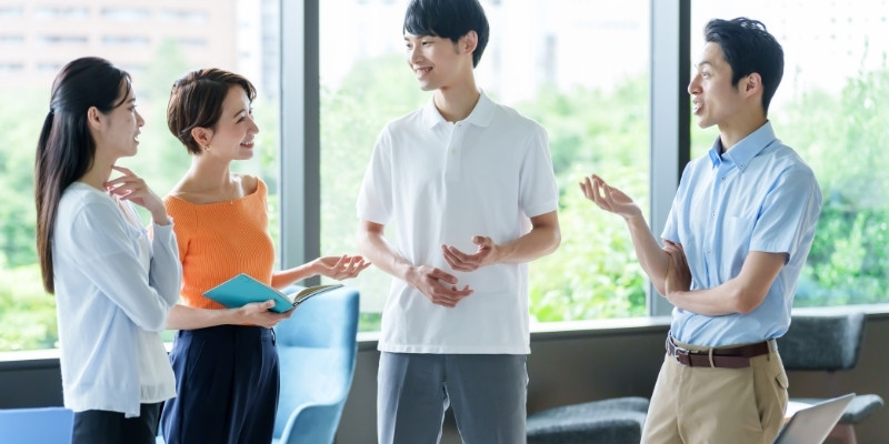 職場で談笑する男女4人の写真