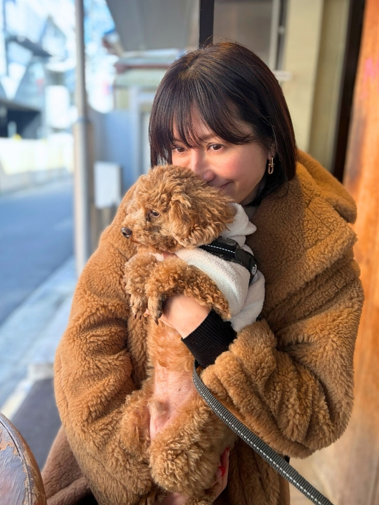 テディベアコートを着て犬を抱きあげている飯島さんの写真