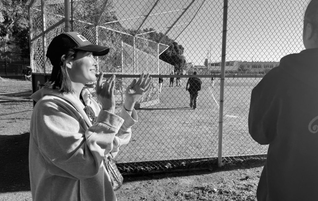 グラウンドで息子さんを見守るキャップをかぶった高木さんの写真
