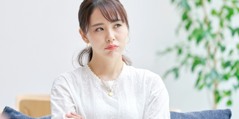目線を左上にやって腕を組み、考え事をしている女性の写真