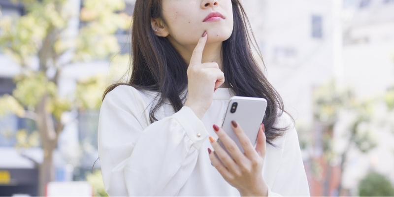 スマホを片手に悩む女性の写真