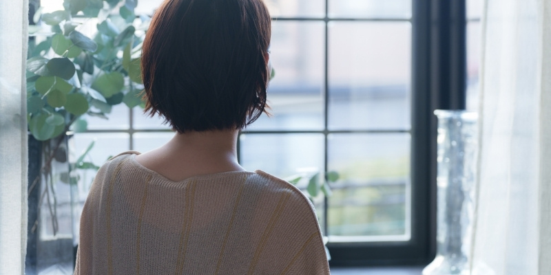 窓の外を眺める女性の背中の写真