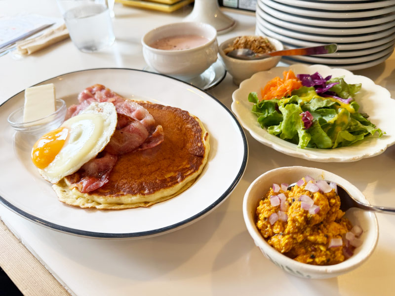 ベーコンと目玉焼きがのったパンケーキ、サラダ、キーマカレーセットの写真