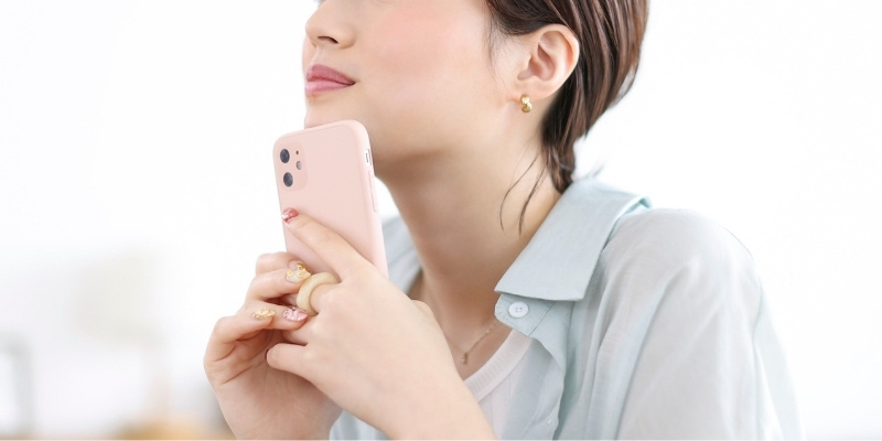 スマホを顎に当てて考え事をしている女性の写真