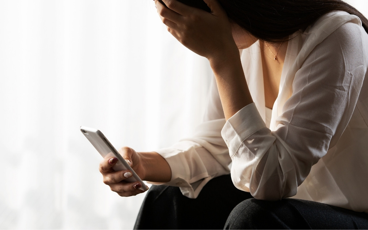 スマホを見て頭を抱える女性の写真