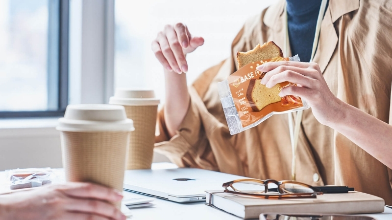 仕事の合間に片手でパウンドケーキを食べる女性の写真
