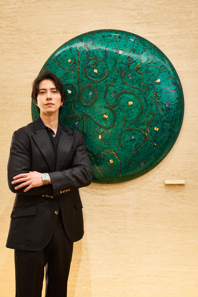 緑色のアートの前に立つ山下智久さん
