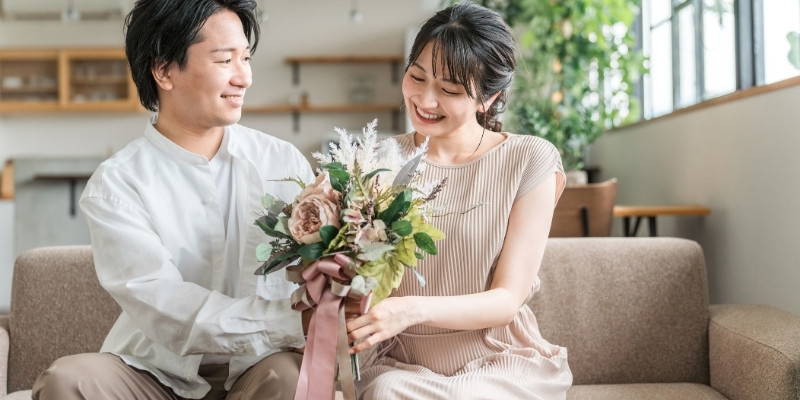 男性に花束をプレゼントされ微笑む女性の写真