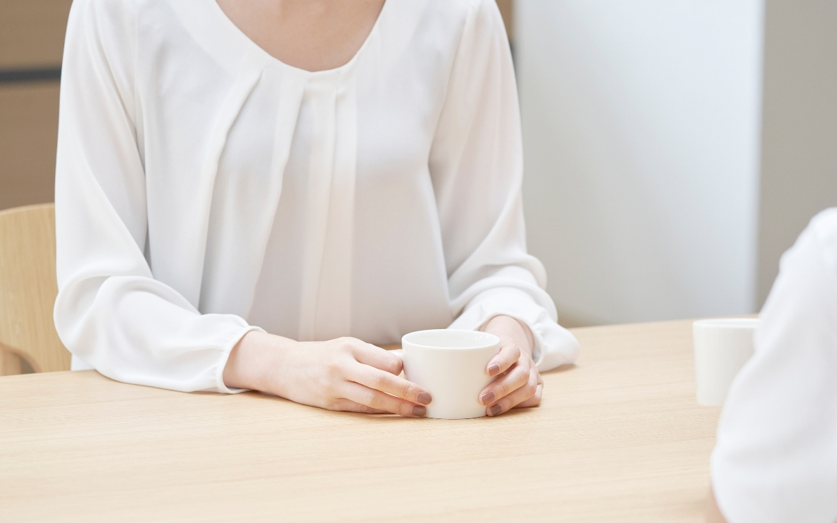 テーブルでコーヒーカップを持ち、相手と向かい合う女性の写真