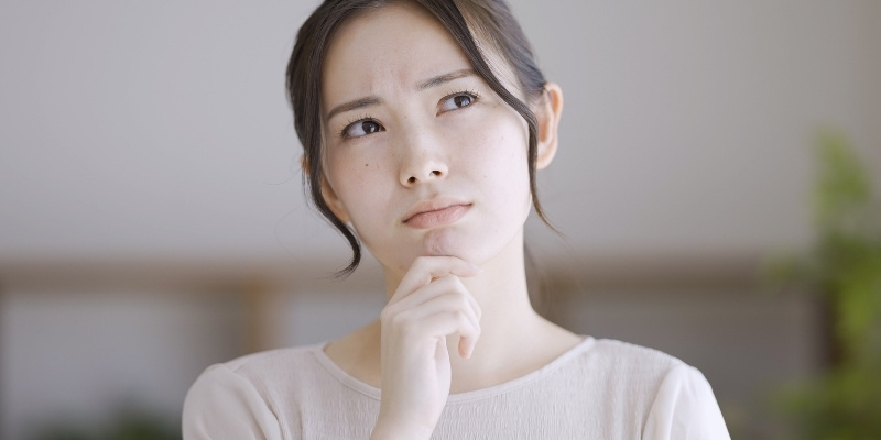 顎に手を当て上を向きながら考え事をする女性の写真