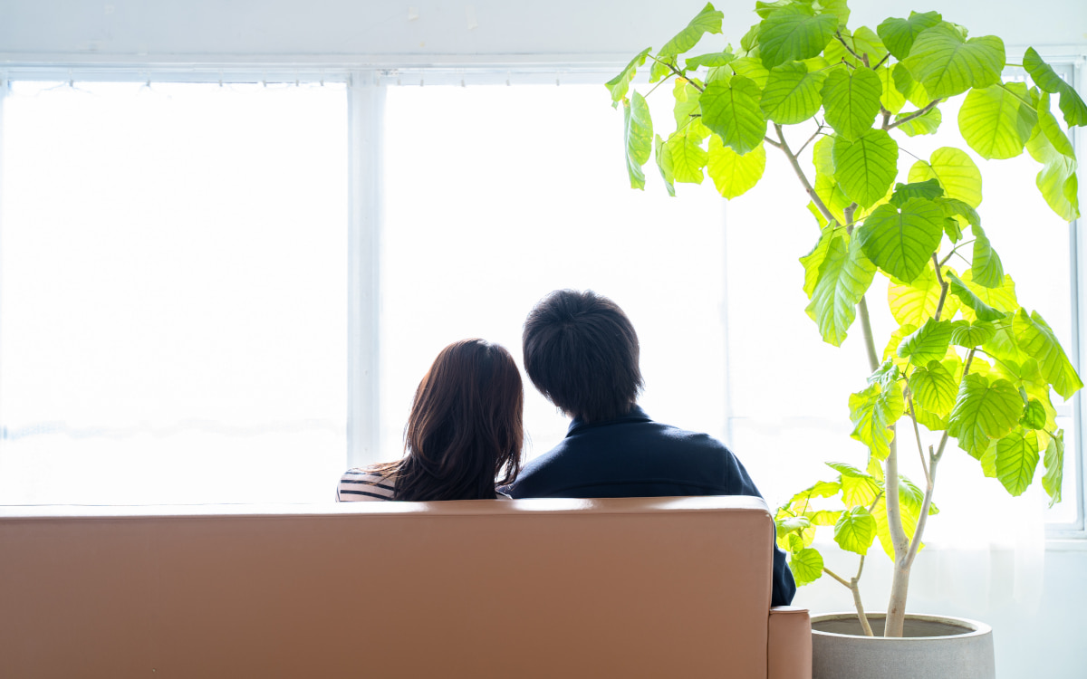 ソファに座って寄り添う男女の後姿の写真