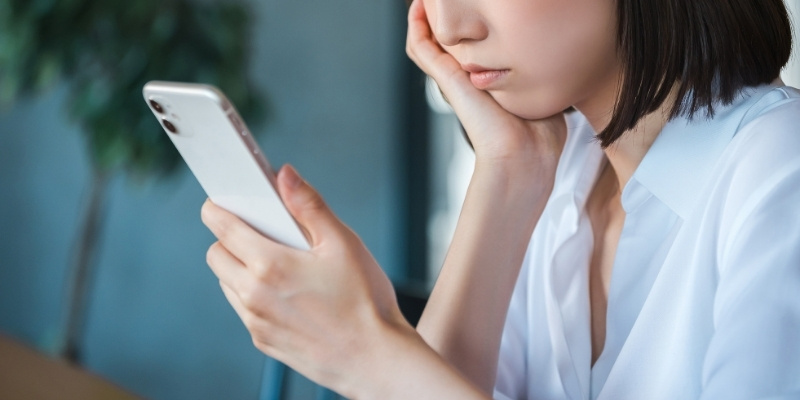 スマホを見ながら考え込む女性の写真