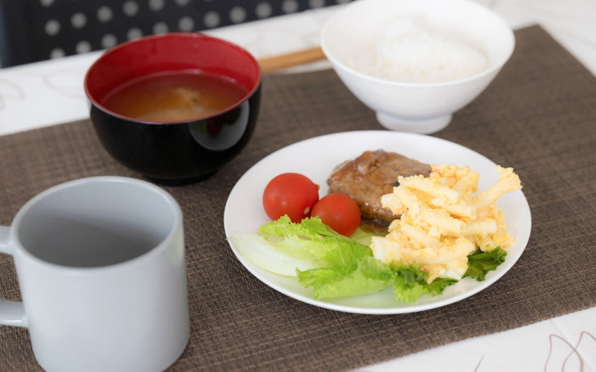 テーブルの上のハンバーグと味噌汁・ご飯・マグカップの写真