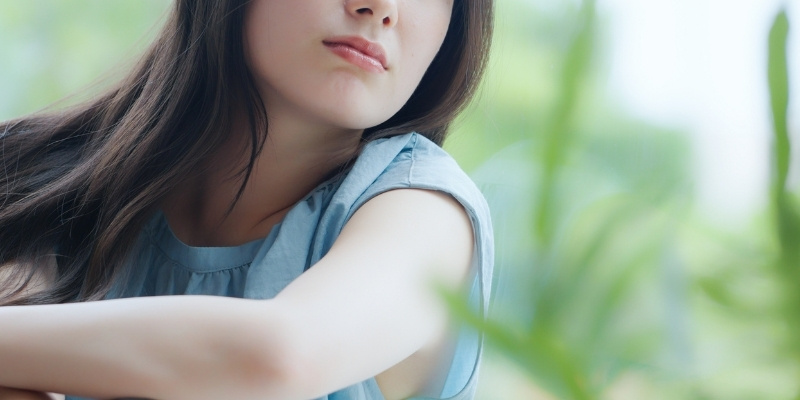 窓に寄りかかって考え事をする女性の写真