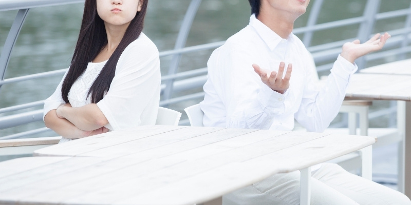 水辺のカフェで怒っている彼女と嘆いている彼氏の写真