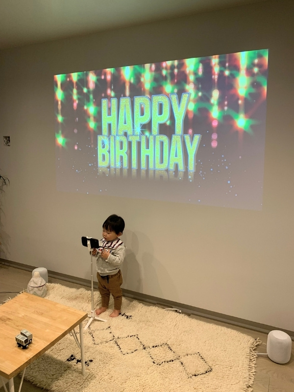 ハッピーバースデーと壁に映し出されており、その下に息子さんが立っている写真