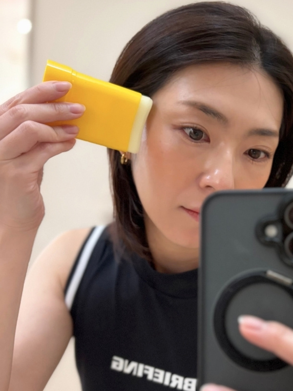 メイクの上から顔にスティックをぬっている写真