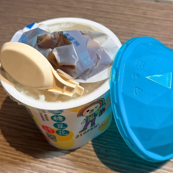 蓋を開けた豆花の写真。折りたたみのプラスチックスプーンと黒糖蜜の袋入り