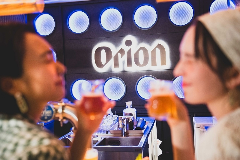 映えるOrionのロゴの前でビールを飲む2人の女性